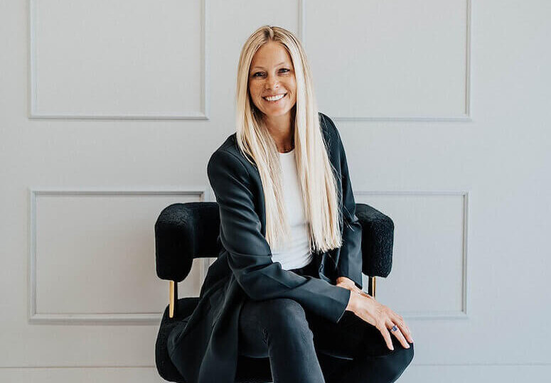 Shayla Gifford sitting on a chair, with her hand on her leg, looking to the camera and smiling